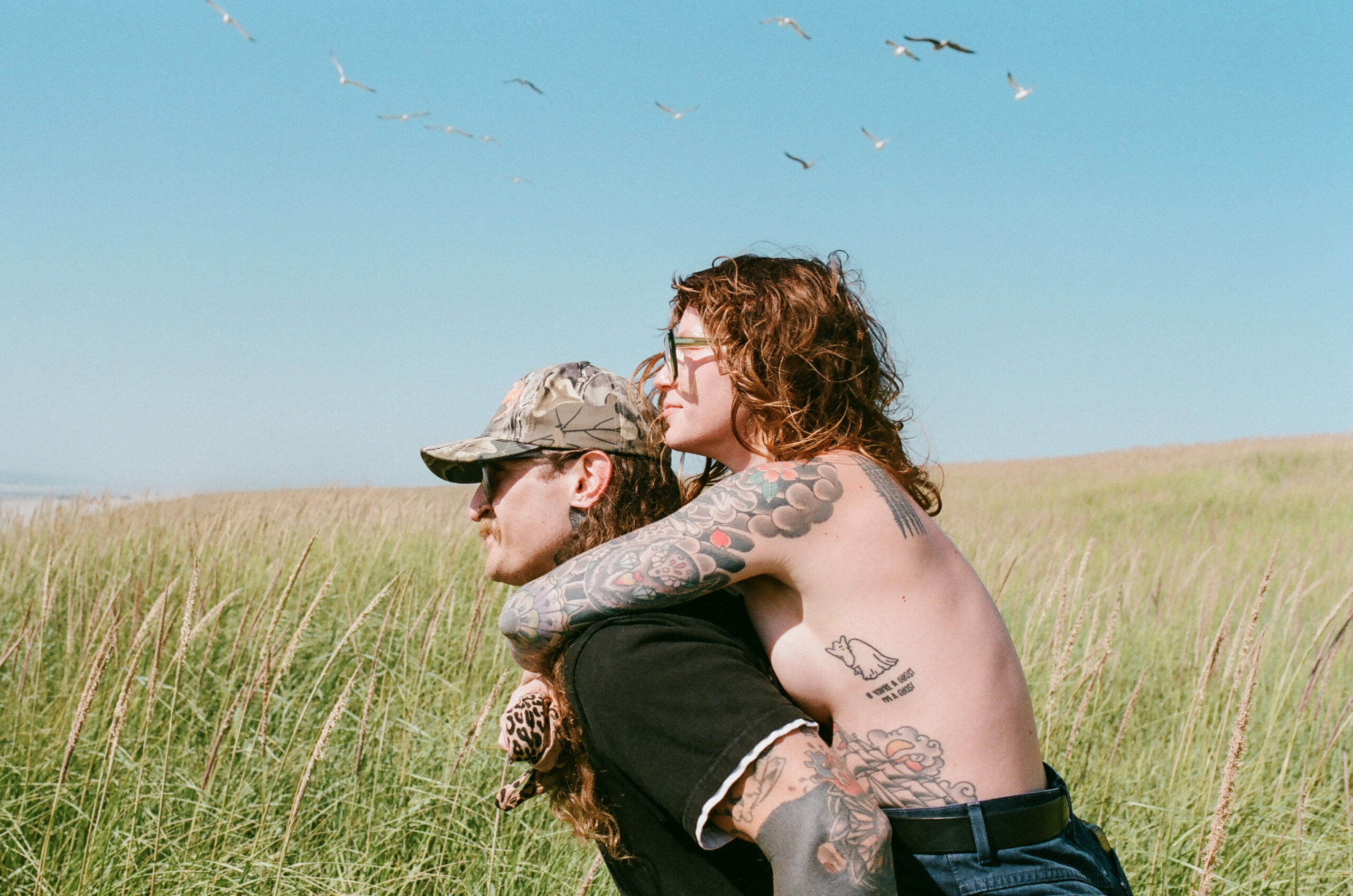 couple standing in an open grassy field with a bright blue sky and seagulls