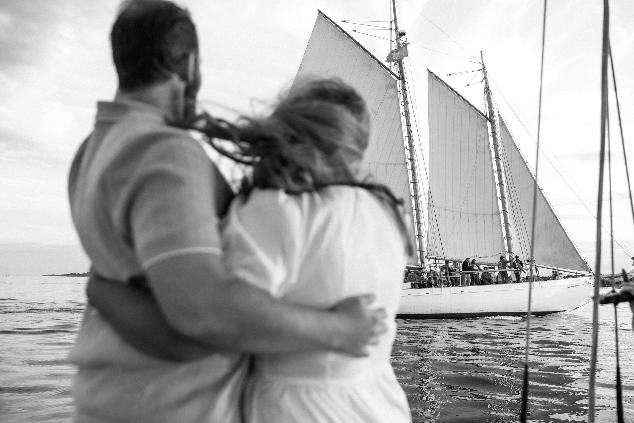 candid photo of couple waving at a sailboat passing by in portland maine 
